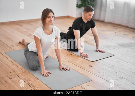 Junger Mann und brünette Frau Yoga sitzen auf grauem Teppich im Zimmer am Tag Stockfoto