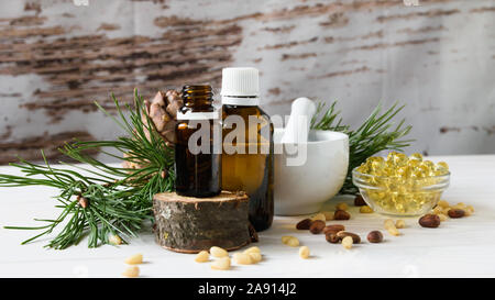 Zusammensetzung der Zeder Öl mit Pinienkernen auf dem Hintergrund einer Zweigniederlassung mit einem Pine Cone, auf einem hellen Hintergrund Stockfoto