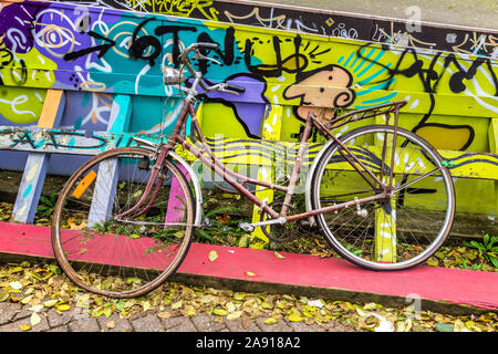 Abgebrochene Fahrrad neben bemalte Zaun - Brüssel, Belgien. Stockfoto