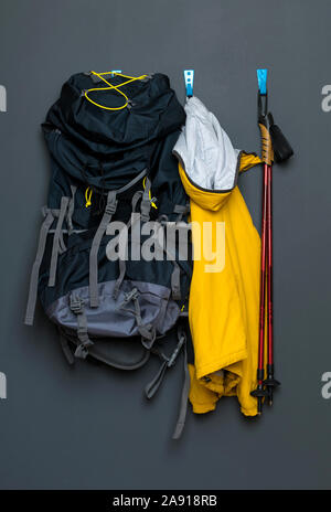 Nordic Walking Stöcke hängen an einer grauen Wand mit einem Rucksack für den Tourismus und eine Jacke. Konzept des gesunden Lebens. Stockfoto