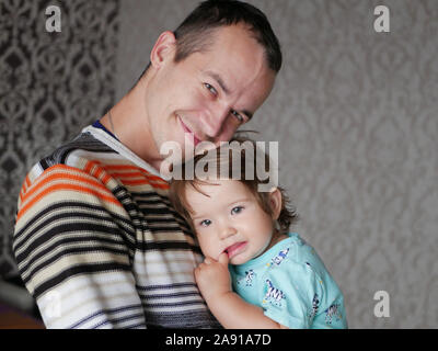 Liebevoller Vater umarmt das Kind in seine Arme. Baby 0-1 Jahr alt. Väterliche Liebe. Die Beziehung von Vater und Sohn. Ein liebevoller Vater hält, ein Kind in seine Stockfoto
