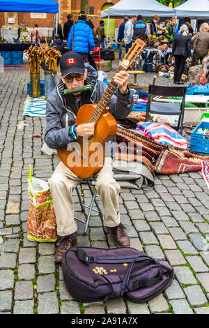 Alter Mann mit Gitarre und Mundharmonika auf Flohmarkt - Brüssel, Belgien. Stockfoto