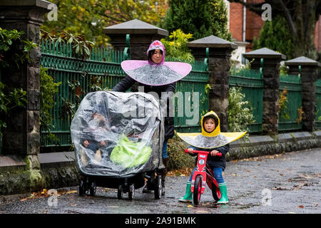 Parichat Sae-Lao Spaziergänge im Regen mit ihrer Tochter Daisy und anderen Kindern in Belfast nach schweren nächtlichen Regen lokalisierten Überschwemmungen in Teilen Nordirlands verursacht. Stockfoto