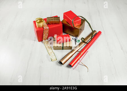 Verpackung Weihnachtsgeschenke in Papier Konzept. Menge Kartons, Bänder, Schere, Klebeband auf weißem Holzfußboden. Stockfoto