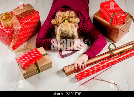 Top down Sicht der unkenntlich Frau Hausfrau müde der Verpackung Weihnachtsgeschenke und liegen auf dem Boden. Saisonale Urlaub Depression Konzept. In Stockfoto