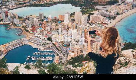 Mädchen kletterte bis auf Penon d'Ifach. Genießen Sie Blick auf die Stadt von oben, stand auf der Spitze des Berges nimmt Foto von Stadtbild und Landschaft. Tourismus Konzept Stockfoto