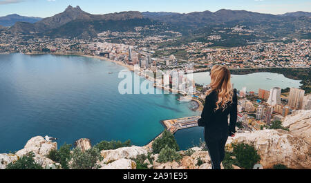 Ansicht von hinten Frau kletterte bis auf die Spitze der Penon d'Ifach genießen Sie malerische Ansicht Mittelmeer, Gebirge, stadtbild Landschaft. Tourismus, Spanien Stockfoto