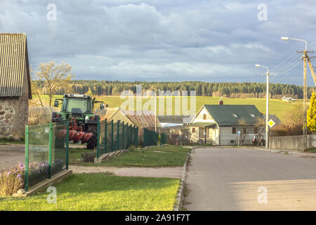 Dorfstraße. Ein Traktor mit Pflug steht in der Nähe einer Scheune. Podlasien, Polen. Stockfoto