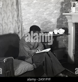 1950, historische, eine ausländische ausländischen Studenten aus einem afrikanischen Land in seiner bedsit studieren, England, Großbritannien sitzen. Stockfoto