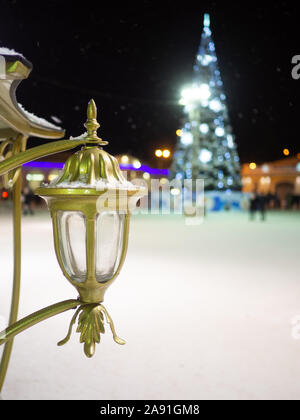 Dekorative Golden Lantern bestäubt mit Schnee auf einer Nacht Ort Straße im Winter. Im Hintergrund ein Defokussierten Weihnachtsbaum. Traditionelle Symbole des Stockfoto