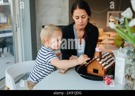 Mutter mit Sohn dekorieren Gingerbread House Stockfoto