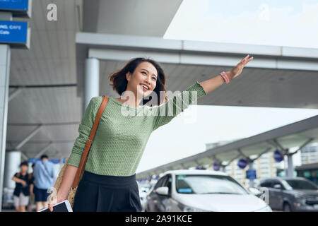 Eine junge asiatische Frau, ihr Auto, ihr über eine Fahrt hageln App gebucht und winkte ihn unten Stockfoto