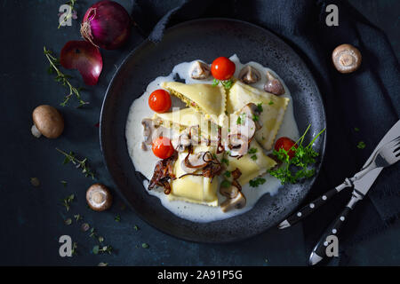 Schwäbische Gemüse Ravioli (so genannte 'Maultaschen') mit Pilzen und Sahnesauce gebratene Zwiebelringe, dunkel und Moody Stil Stockfoto