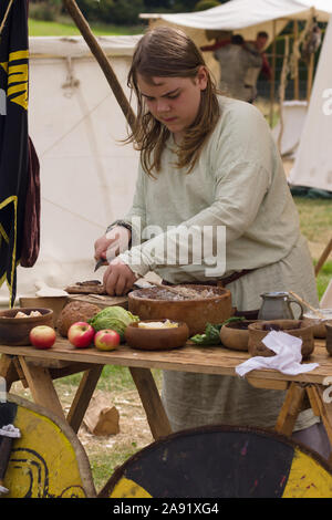 Frau gekleidet in mittelalterlichen Kostüm Vorbereiten der Nahrung zu einem Re-enactment Camp Stockfoto