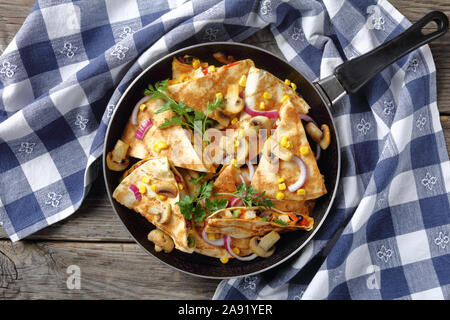 In Scheiben geschnitten Quesadilla mit Hähnchen, Tomaten, Mais, roten Bohnen, Pilze und Cheddar Käse in einer Pfanne bei einem rustikalen Holztisch mit Küchenpapier Stockfoto