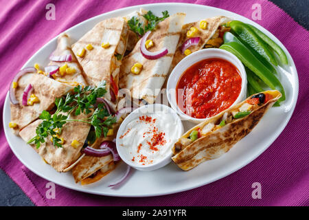 Mexikanischen Chicken Quesadilla mit Gemüse, Maiskörner, shredded Cheddar Käse, Oliven und Champignons Füllungen auf eine weiße, ovale Servierplatte mit Tomate s Stockfoto