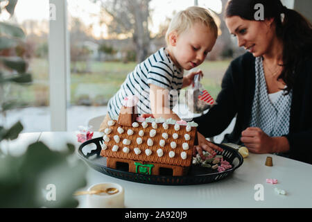 Mutter mit Sohn dekorieren Gingerbread House Stockfoto