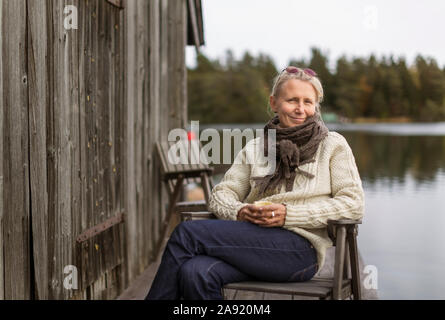 Lächelnde Frau sitzt am See Stockfoto