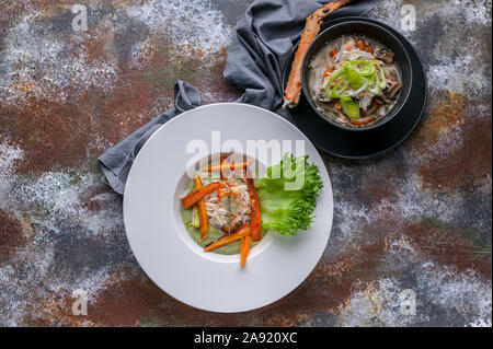 Close-up-Salat mit seespinne Fleisch, Suppe mit Schnee Krebsfleisch, udon Nudeln und Gemüse. Serviert auf einem grauen Serviette und eine rostige Hintergrund. Ansicht von oben Stockfoto