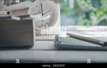 Klasse Zimmer in Natur Hintergrund mit grünen Bücher, Bleistifte, Wecker, auf einem weißen Tisch Stockfoto