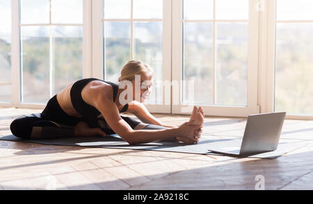 Flexible girl Yoga zu Hause, beim Laptop Bildschirm schaut Stockfoto