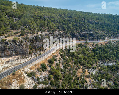 Eine kurvenreiche Gebirgsstraße verläuft entlang dem Rand eines bewaldeten Schlucht. Luftaufnahme. Stockfoto