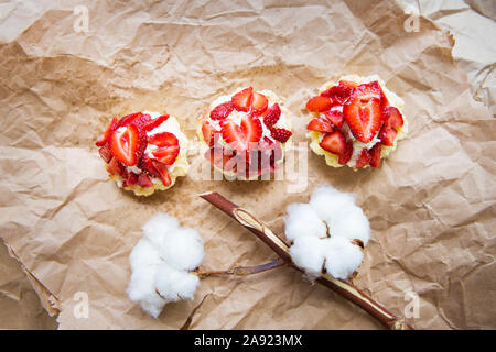 Schöne kleine Kuchen mit Erdbeeren zusammen mit einem Zweig der Baumwolle liegt auf Kraftpapier. Stockfoto