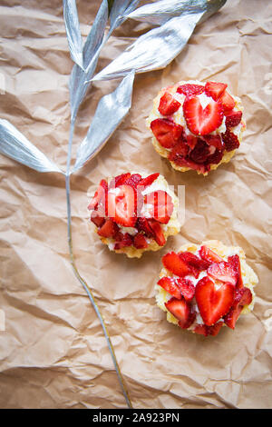 Schöne kleine Kuchen mit Erdbeeren zusammen mit einem Zweig auf Kraftpapier. Stockfoto