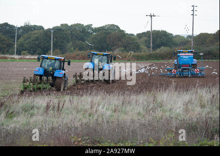 Blau New Holland T7 Traktoren, Pflügen und Säen, der Saatgut in einem Feld auf Hayling Island England Stockfoto