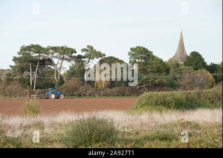 Eine blaue New Holland Traktor Pflügen eine neben der St. Mary's Kirche abgelegt auf Hayling Island England Stockfoto