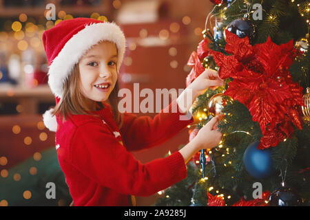 Adorable kleine Mädchen schmücken Weihnachtsbaum mit bunten Blasen Stockfoto