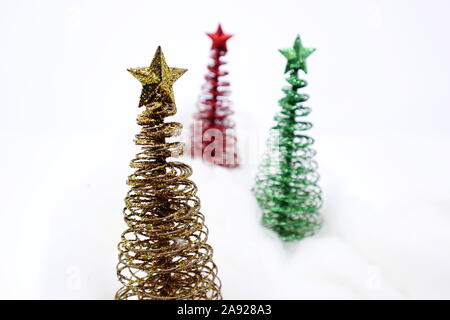 Drei Spielzeug Weihnachtsbäume (grün, rot und Gold) mit Start auf der Oberseite, auf weißem Hintergrund mit weißer Wolle künstlichen Schnee Stockfoto