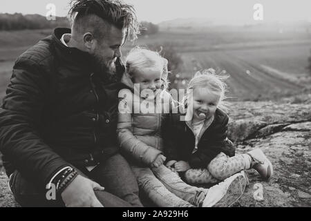 Zwei Töchter und ein Vater sitzt auf einem Hügel Stockfoto