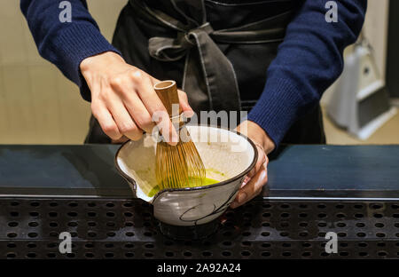 Weibliche barista Hände vorbereiten Matcha Tee auf eine Schüssel, den Sie mit einem Bambusbesen in Busan, Korea Stockfoto