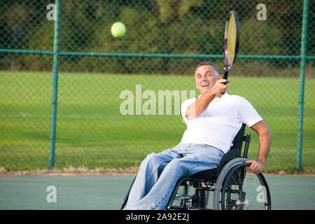 Älterer Mann, der im Rollstuhl sitzt und Tennis spielt. Stockfoto