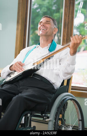 Reifer Mann sitzt in einem Rollstuhl mit einem Rückenmark Verletzung und eine E-Gitarre spielen Stockfoto