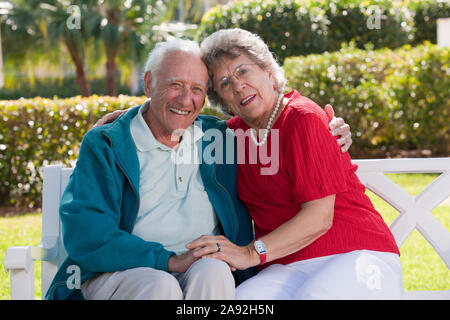 Seniorenpaar mit Arm um auf einer Parkbank sitzend Stockfoto
