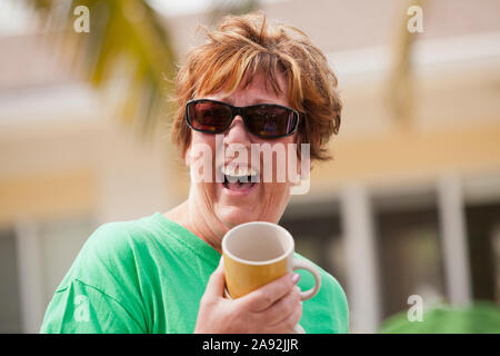 Ältere Frau hält eine Tasse und lacht Stockfoto