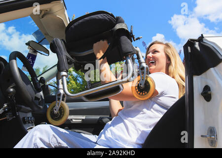 Frau mit Verletzungen des Rückenmarks ziehen Stuhl vom Rollstuhl in ihrem adaptiven Fahrzeug Stockfoto