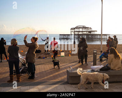 Seifenblasen machen auf der Strandpromenade mit Menschen und Hunden beobachten und West Pier im Hintergrund; Brighton, East Sussex, England Stockfoto