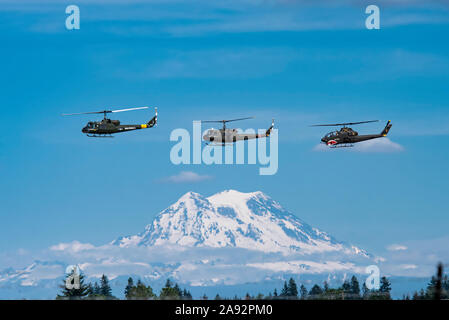 Ein Paar UH-1 Huey Helicopters und eine AH-1 Cobra fliegen in Formation mit Mount Rainier im Hintergrund, 2019 Olympic Air Show, Olympic Airport Stockfoto