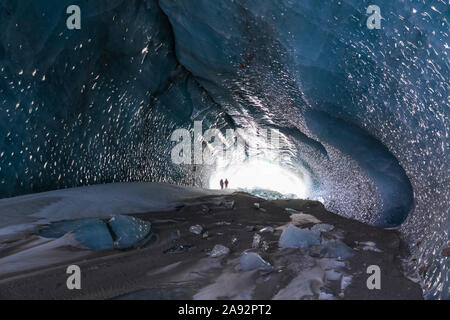 Ein Paar Wanderer stehen silhouetted im Eingang einer Black Rapids Gletscher Eishöhle; Alaska, Vereinigte Staaten von Amerika Stockfoto