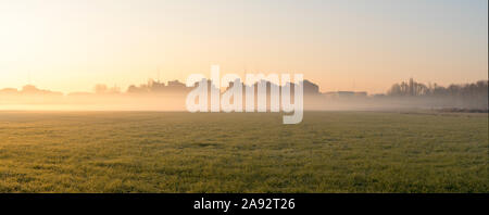 Stadtbild bei Sonnenaufgang. Häuser am Rande der Stadt mit Nebel im Morgengrauen im Winter. Tritt Rauch aus den Schornsteinen. Stockfoto