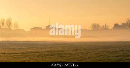 Stadtbild bei Sonnenaufgang. Häuser am Rande der Stadt mit Nebel im Morgengrauen im Winter. Tritt Rauch aus den Schornsteinen. Stockfoto