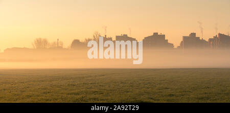 Stadtbild bei Sonnenaufgang. Häuser am Rande der Stadt mit Nebel im Morgengrauen im Winter. Tritt Rauch aus den Schornsteinen. Stockfoto