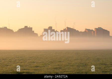 Stadtbild bei Sonnenaufgang. Häuser am Rande der Stadt mit Nebel im Morgengrauen im Winter. Tritt Rauch aus den Schornsteinen. Stockfoto