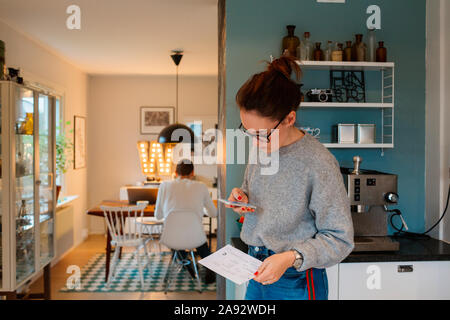 Junge Frau mit Smartphone in der Küche Stockfoto