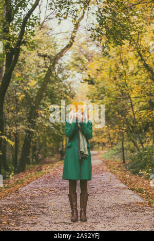 Frau, die ihr Gesicht mit Fallen leafs Während genießt im Herbst und die Zeit im Park. Stockfoto