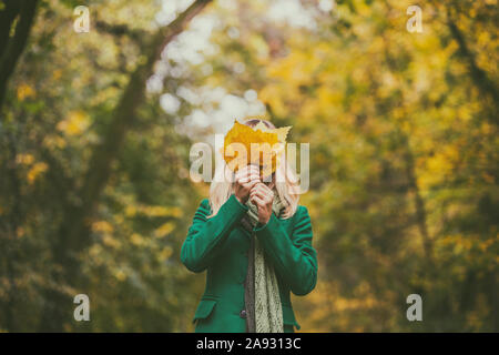 Frau, die ihr Gesicht mit Fallen leafs Während genießt im Herbst und die Zeit im Park. Stockfoto