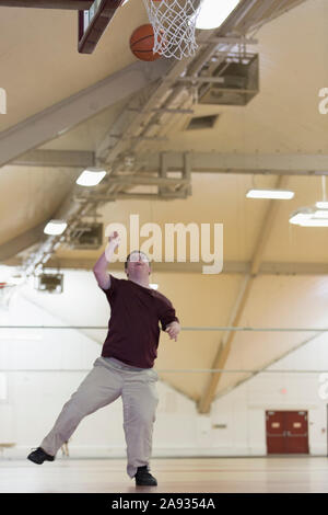 Junger Mann mit Down-Syndrom spielt Basketball in der Schule Turnhalle Stockfoto